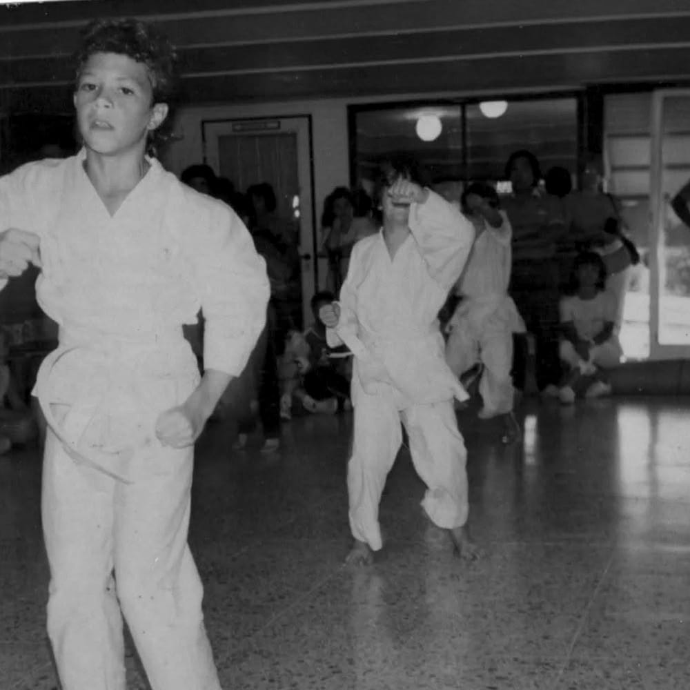 Chicos en clase de taekwondo, con familias mirando de fondo